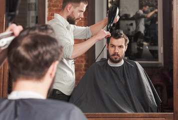 Young handsome barber making haircut of attractive man in barbershop