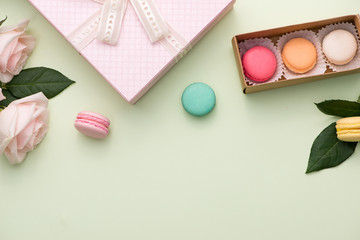 French macaroons. Many variegated sweet macarons in box with bouquet of pink roses on the table