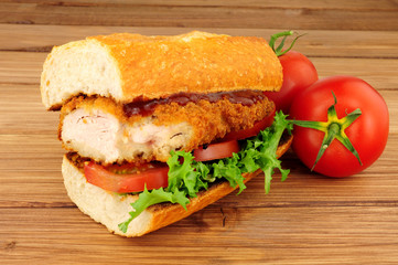 Southern fried chicken steak sandwich with fresh salad on a wood background