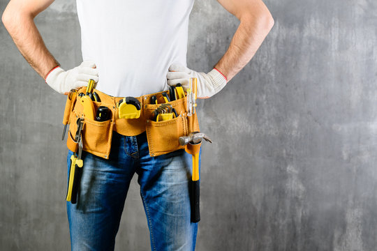 unknown handyman with hands on waist and tool belt with construction tools against grey background with copyspace for text. DIY tools and manual work concept