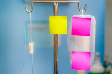 Yellow and pink reminder sticky note on Saline solution for intravenous infusion in hospital, empty space for text with light from window.