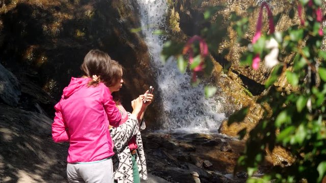 Friends posing taking pictures on the phone by the waterfall. 3840x2160