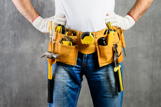 unknown handyman with hands on waist and tool belt with construction tools against grey background. DIY tools and manual work concept