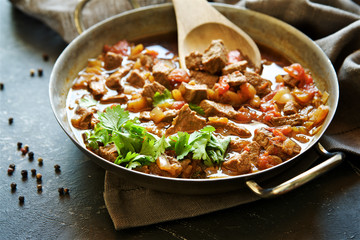 Stewed beef with vegetables in. Dark scratched background 
