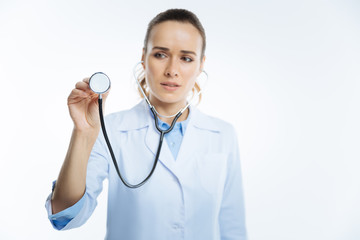 Focused female looking doctor listening to heart with stethoscope