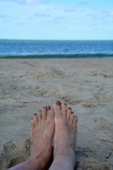 Sandige Füße mit roten Fußnägel am Strand mit unscharfen Meer im Hintergrund