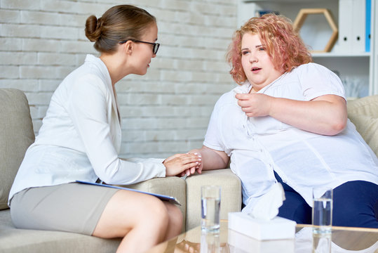 Portrait of crying obese woman opening up to female psychiatrist during therapy session  on mental issues