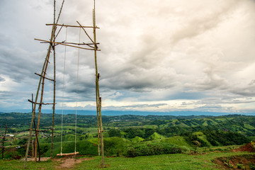 Old bamboo swing on the mountain with cloudy sky and village view. 