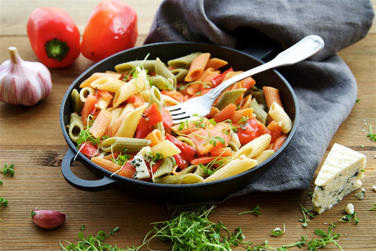 Multicolored penne pasta with vegetables. Roasted red bell pepper, tomatoes, garlic and young parsley 
