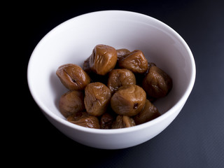 Umeboshi plums from Japan in white bowl, fermented and salted and placed in a honey syrup. Isolated on black background