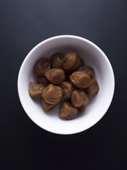 Umeboshi plums from Japan in white bowl, fermented and salted and placed in a honey syrup. Isolated on black background