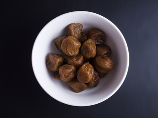 Umeboshi plums from Japan in white bowl, fermented and salted and placed in a honey syrup. Isolated on black background