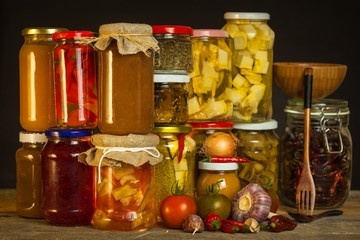 Jars with marinated food and organic raw vegetables. Preserved vegetables on wooden background. Various marinaded food. Life on a rural farm.
