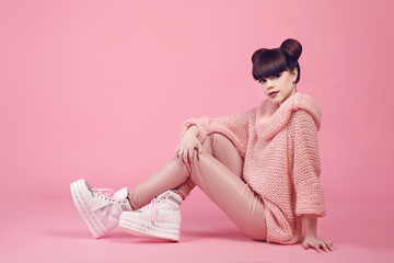 Obraz na płótnie Canvas Fashion studio teen look style in shoes. Fashionable young girl wears in wool sweater and leather pants sitting on the floor isolated on pink background.
