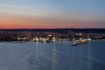 Night lights from the city and the sea port in Varna, Bulgaria at twilight with beautiful striped sky and water