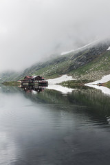 Nature landscape of amazing glacier lake Balea with house on shore and Fagaras mountains with white strips of snow reflected in the water at Carpathians, Romania