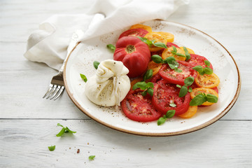 Fresh tomato salad with burrata cheese (mozzarella) and basil. White wooden rustic table
