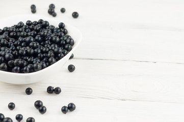 Many fresh ripe blackcurrant in white bowl and scattered on old white rustic wooden planks