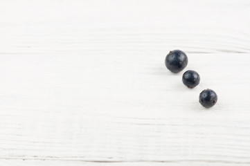 Three fresh ripe blackcurrant on old white rustic wooden planks