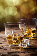 Whiskey with ice in glasses on rustic wood background