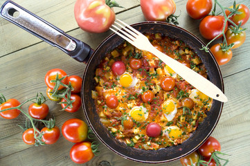 Shakshouka with pita bread on the pan. In the middle East, a traditional dish. Scrambled eggs with tomatoes, peppers, vegetables and herbs. Shakshuka on the table. The view from the top.
