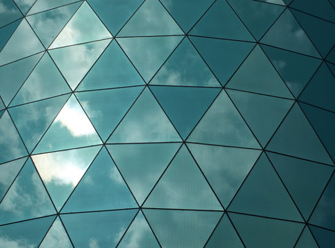 angular mirror cladding on a modern structure with reflected sky and clouds