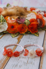 Orange handmade flower circle for newborn babies and headband with fake flowers lying on wooden plank floor