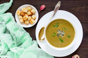 Vegetable cream soup with spinach and potatoes in a white bowl with garlic croutons on a dark wooden background. Dietary vegetarian menu. Proper nutrition.