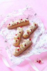 Eclairs with Vanilla Pastry Cream and Cream Cheese Filling, decorated with red currants and white chocolate hearts, on light pink background.