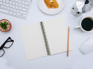 White office desk with computer, notebook, small plant, cup of coffee, coffee maker, croissant. Top view and copy space for mockup, website banner, background, presentation and marketing material.