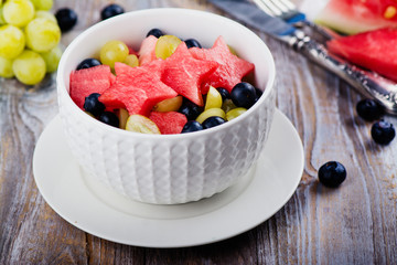 Fresh summer watermelon salad with blueberry and grapes on wooden table. Copy space
