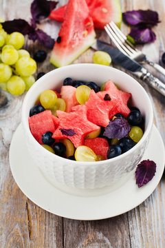 Fresh summer watermelon salad with blueberry and grapes on wooden table. Copy space