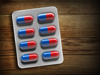 Red and blue pills in a blister on a wooden background