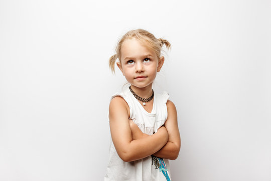 Little girl in white dress with crossed arms looks up on white background