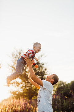 Man throws his son up posing on the field in lights of evening sun