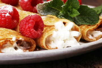Homemade crepes served with fresh raspberrries and powdered sugar on rustic wooden table