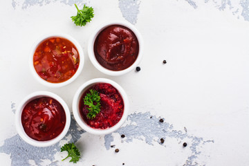 Bowls of various tomato sauces on white stone table. Top view. Copy space