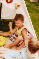 Children sit under white tent with toy birds on picnic