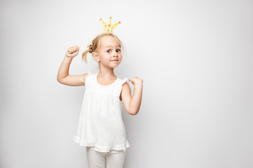 Beautiful little girl with paper crown posing on white background at home.