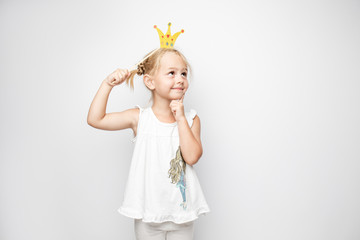 Beautiful little girl with paper crown posing on white background at home.