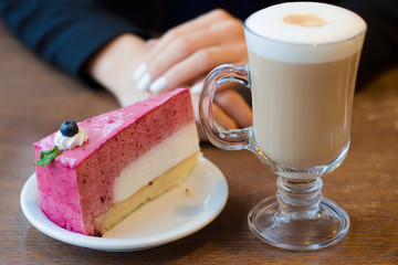 Young beautiful woman drinks coffee latte with foam on the table cake