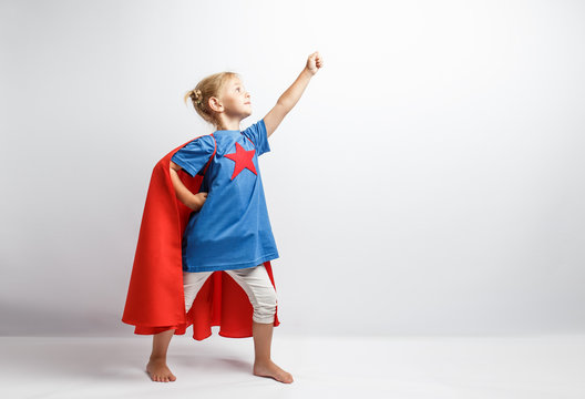Little girl dressed like superhero standing alongside the white wall.