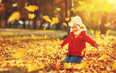 happy child girl throws autumn leaves and laughs