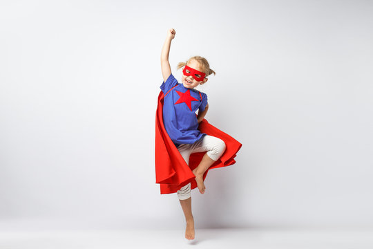Very excited little girl dressed like superhero jumping alongside the white wall.