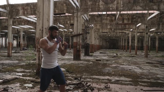 Slow motion shot of muscular athlete doing shadow boxing exercise in an old abandoned building.