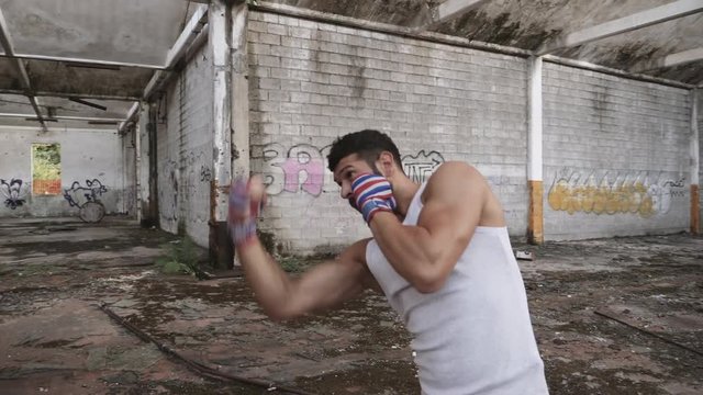 Muscular male boxer doing shadow boxing exercise in an old abandoned building.