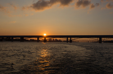 Fototapeta na wymiar The silhouette of the bridge against the setting sun and the river