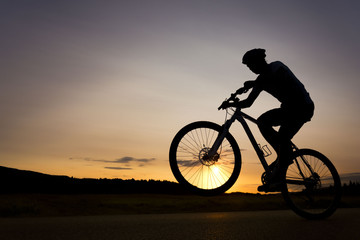 Silhouette of boy on the bike. Young cyclist is jumping on his bike during susnet.  Fore wheel is over the horizon.