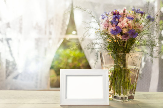 Empty white frame and vase with flowers