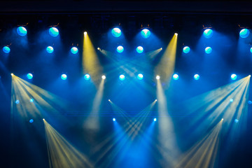 Verlichtingsapparatuur op het podium van het theater tijdens de voorstelling. De lichtstralen van de schijnwerper door de rook. Blauwe en gele lichtstralen.